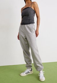 Grå sweatpants med elastiska manschetter, i kombination med en svart denimtopp i crop-modell med metallicdetaljer. Vita och marineblå sneakers kompletterar outfiten.