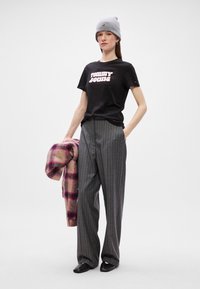 Μαύρη μπλούζα με "TOMMY JEANS" σε ροζ, γκρι ριγέ παντελόνι σε φαρδιά γραμμή, και καρό παλτό σε ροζ, μωβ και κρέμα. Γκρι σκούφος και μαύρα παπούτσια.