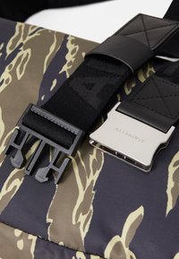 Borsa con motivo camouflage caratterizzata da una superficie in nylon testurizzato, una tracolla nera regolabile e una fibbia in metallo argentato con marchio inciso.