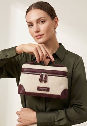 Femme en chemise olive tenant un sac à main Diana&Co Firenze crème et bordeaux avec poignée supérieure et double fermeture éclair.