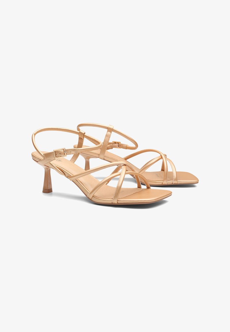 Sandalias desnudas con tiras finas metálicas y un pequeño tacón cónico. Textura de cuero suave con un diseño minimalista.