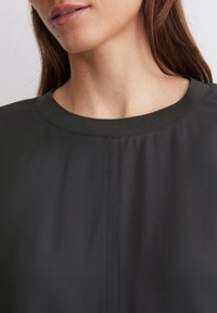 Dark gray, lightweight fabric top with a round neckline and visible stitching details. Smooth texture with a relaxed fit design.