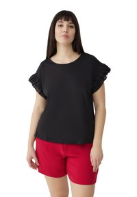 Top corto nero a maniche corte con bordi arricciati, scollo rotondo e texture morbida, abbinato a pantaloni corti rossi. Entrambi i capi hanno una vestibilità rilassata.