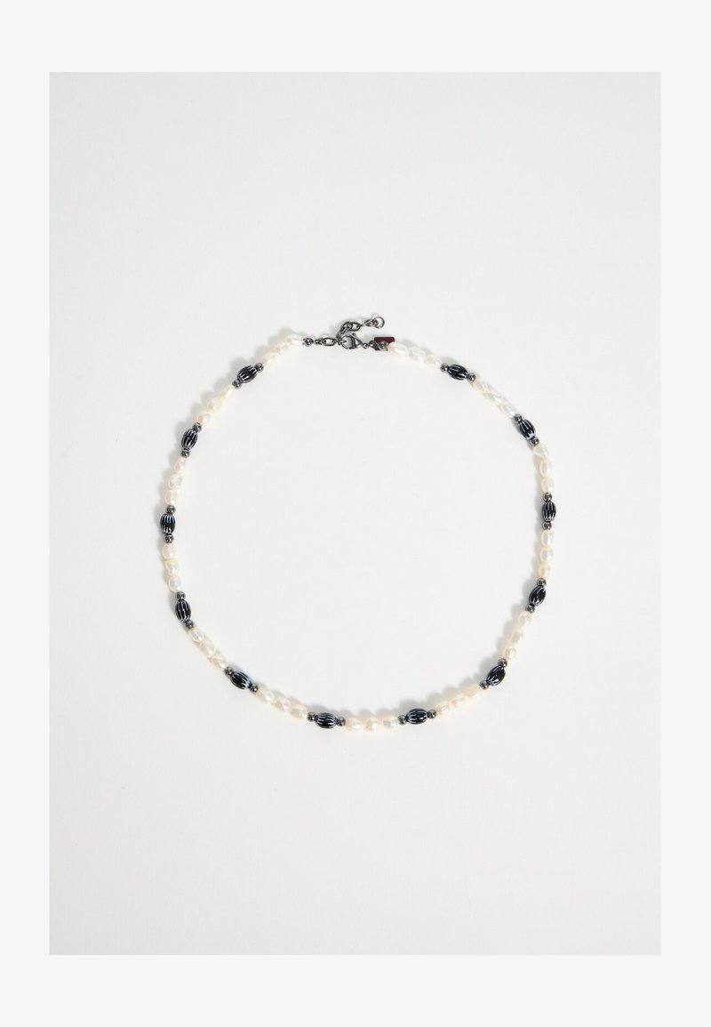 Collier avec des petites perles blanches alternées et de plus grosses perles ovales noires avec des rayures blanches, sécurisé par un petit fermoir en métal.