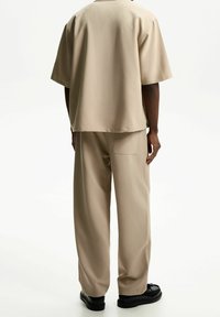 Beżowa, luźna koszula z krótkim rękawem w połączeniu z pasującymi spodniami o szerokich nogawkach. Gładka faktura, minimalistyczny design oraz detal w postaci tylnej kieszeni.