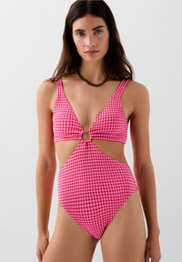 Roze gingham badpak met een diepe V-hals, cirkelvormige uitsnede op de taille, brede bandjes en hoge beenopeningen. Glad stofoppervlak.