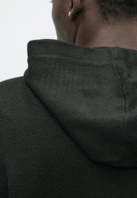 Dark gray hooded sweater featuring a textured knit pattern, with a visible hood and seam detailing at the back.