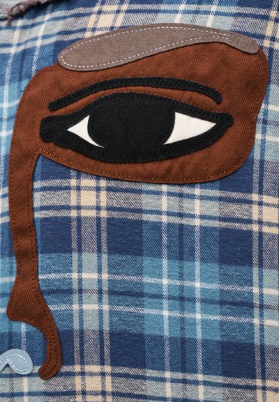 Καρό πουκάμισο σε αποχρώσεις μπλε, τιρκουάζ και μπεζ με μεγάλο κεντητό καφέ πατς ματιού και αντιθετικό μαύρο περίγραμμα ματιού.