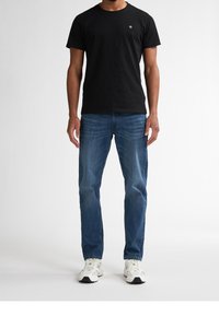 Camiseta de algodón negra con cuello redondo, combinada con unos pantalones vaqueros de mezclilla azul claro. Corte holgado, llevada con zapatillas blancas con detalles en negro.