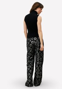 Zwarte mouwloze coltrui gecombineerd met high-waisted, bloemmotief-pantalon in zwart en grijs, met een geweven stofontwerp.