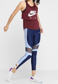 Top corto bordeaux con logo bianco "NIKE AIR", abbinato a leggings blu navy e azzurri con dettagli in rete e blocchi di colore.