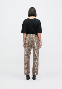 Μαύρο κοντομάνικο μπλ�ουζάκι σε συνδυασμό με παντελόνι φαρδιάς γραμμής με λεοπάρ σχέδιο σε μπεζ και καφέ αποχρώσεις, με υφή υφάσματος και αντιθετικά μοτίβα.