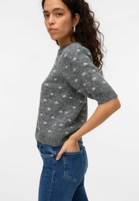 Grå stickad tröja med korta ärmar och vita prickar, med en avslappnad passform och mjuk textur. Bärs med blå denimjeans.