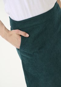 Jupe en velours côtelé teal avec une texture lisse et une poche latérale. La taille est ajustée et présente des détails de couture subtils.