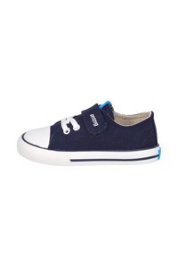 Zapato de lona navy con punta de goma blanca, cierre con cordones y correa de Velcro. Presenta un acento azul en el talón y una suela blanca con una raya navy.