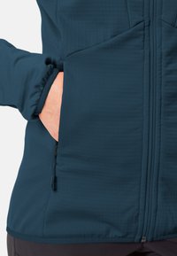 Marineblauwe ritsjack in een zachte, gestructureerde stof. Voorzien van een zijzak en subtiele geribbelde accenten bij de manchetten en de zoom.