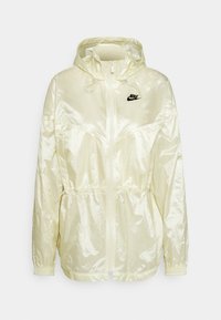 Ljusgul, glänsande nylonjacka med huva, dragkedja fram, elastiska ärmslut, dragsko i midjan och en liten svart Nike-logotyp på bröstet.