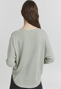 Lichtgroene, gestructureerde gebreide trui met een relaxed fit, brede halslijn en drop shoulders. De zoom is licht gebogen.