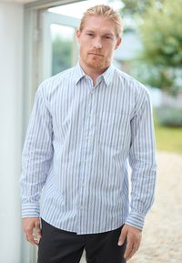 Gestreifte Button-Up-Bluse in Hellblau und Weiß, lange Ärmel, eine Brusttasche, lässiger Schnitt, kombiniert mit dunklen Hosen.