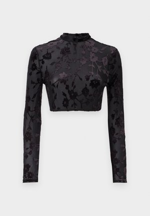 Sort langærmet crop top med høj hals, der har et blomster velourmønster på gennemsigtigt stof, der fremhæver den intrikate detaljering og tekstur.