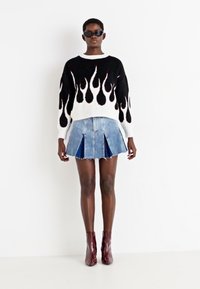 Svart-hvit strikkegenser med flamme-mønster, kombinert med en denim plisserte skjørt. Modellen har på seg runde solbriller og burgunderrøde ankelstøvletter.