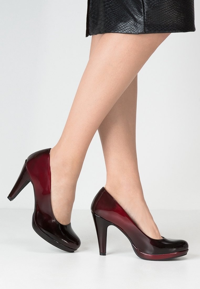 Escarpins en cuir verni de couleur rouge profond, à la forme légèrement courbée, avec une finition brillante. Présente une plateforme et un talon aiguille.