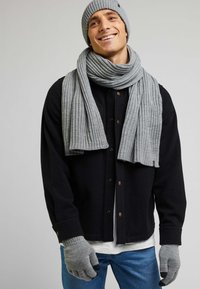 Szary, żeberkowany beanie, szalik i rękawiczki w połączeniu z czarną koszulową kurtką oraz niebieskimi dżinsami. Dodatki to m.in. bezpalcowe końcówki rękawiczek oraz tekstura.