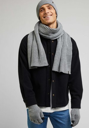 Szary, żeberkowany beanie, szalik i rękawiczki w połączeniu z czarną koszulową kurtką oraz niebieskimi dżinsami. Dodatki to m.in. bezpalcowe końcówki rękawiczek oraz tekstura.