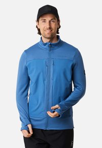 Blaues Zip-Jacke mit strukturiertem Muster, hohem Kragen, zwei vorderen Reißverschlusstaschen und Daumenlöchern an den Ärmeln. Hergestellt aus leichtem Material.