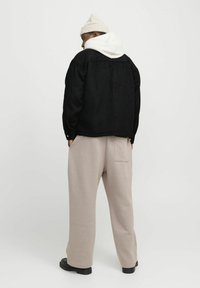 Veste en polaire noire avec un sweat à capuche blanc en dessous, associé à des joggings beige et des bottes noires. Tissu texturé ; coupe décontractée.