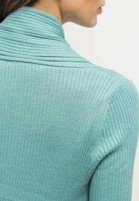 Suéter de cuello alto de canalé en azul verdoso claro con un patrón horizontal texturizado. Diseño ajustado con una tela suave y elástica.