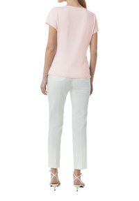 Helles rosafarbenes Kurzarmoberteil mit Rundhalsausschnitt, kombiniert mit enganliegenden weißen Hosen. Das Outfit wird durch sandalen mit hohen Absätzen und Riemchen ergänzt.