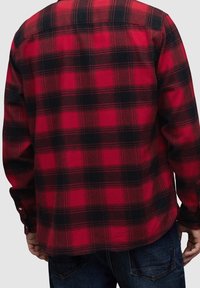 Camicia di flanella a quadri rossi e neri con maniche lunghe, polsino con bottoni, orlo arrotondato e tessuto morbido e strutturato.