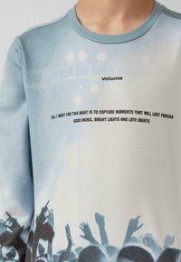 Camisa de manga larga de algodón suave, con un diseño en gradiente azul, gráfico impreso de una multitud y texto en negrita en color negro.