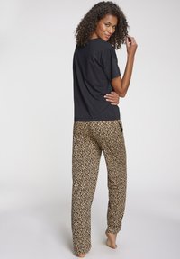 Schwarz kurzärmliges T-Shirt, kombiniert mit beigen Schlafanzughosen mit Leopardenmuster, entworfen für Komfort, mit lockerer Passform und atmungsaktivem Stoff.