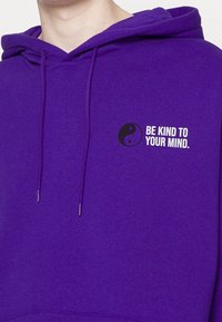 Sudadera morada de mezcla de algodón, que presenta un gráfico de yin-yang y el texto "Sé amable con tu mente" en blanco y negro cerca del pecho.