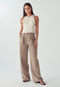 Top beige aderente con zip frontale abbinato a pantaloni beige larghi. Tessuto liscio, design a gamba larga e accenti sottili.
