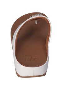 Witte schuifsandalen met een glad bovenwerk, een getextureerde bruine binnenzool en een zilverkleurige strassaccent op de band. Gebogen, open teen ontwerp.