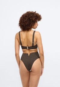 Conjunto de biquíni preto com parte superior estampada, alças grossas e fecho de gancho. Parte de baixo de cintura alta com um corte em v subtil e motivos repetidos.