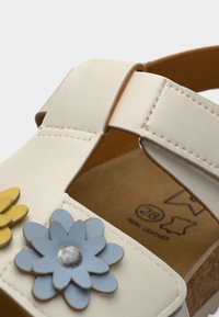 Λευκό δερμάτινο σανδάλι με διακοσμητικά μπλε και κίτρινα λουλούδια, ρυθμιζόμενο λουράκι και φελλό σόλα, μέγεθος 28, με ένδειξη γνήσιου δέρματος στο εσωτερικό.