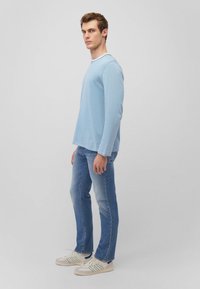 Himmelblaues Langarmhemd mit gerippter Textur, kombiniert mit ausgebleichten blauen Jeans und weißen Sneakers mit grünen Streifenakzenten.