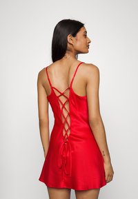 Red satin dress featuring a fitted bodice, thin adjustable straps, and a crisscross lace-up back detail. Flared hemline above mid-thigh.