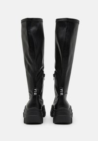 Bottes noires montantes en simili cuir lisse, avec une semelle épaisse et une fermeture éclair sur le côté ; logo "BIA" au talon arrière.