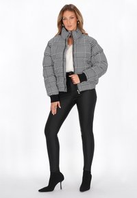 Giacca a vento a quadretti bianco e nero con colletto alto, polsini a coste e chiusura con zip, abbinata a pantaloni neri aderenti e stivaletti con tacco.