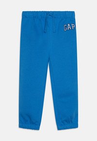 Pantalon de jogging bleu avec une ceinture élastique et un cordon de serrage. Présente des poignets froncés et un logo "GAP" brodé en haut à gauche.