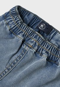Svetlobež denim hlače z elastičnim pasom, zgornjim gumbom in kontrastnim zlatim šivom ob šivih. Gladka tekstura.