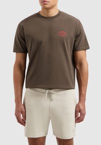 Bruine katoenen t-shirt met een ronde halslijn en korte mouwen, voorzien van een rode grafische print. Gecombineerd met crèmekleurige shorts met koord.