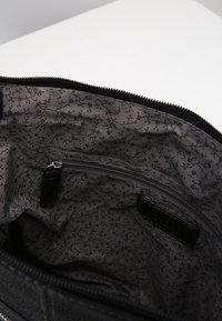 Interno di una borsa in pelle nera con rivestimento in tessuto grigio che presenta piccoli motivi a branche nere e una tasca con zip.