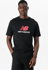 Fekete pamut póló, amelyen egy nagy rózsaszín és fehér "New Balance" logó található. Rövid ujjú, kerek nyakkivágású. Simaság, laza fazon.