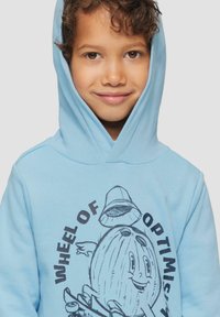 Lichtblauwe hoodie van zacht materiaal, met een afbeelding van een cartoon-kokosnoot met een hoed en de tekst "WIEL VAN OPTIMISME."